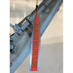 Red Remove Before Flight tag hanging from an aircraft control surface assembly, warning to remove before flight to ensure safety